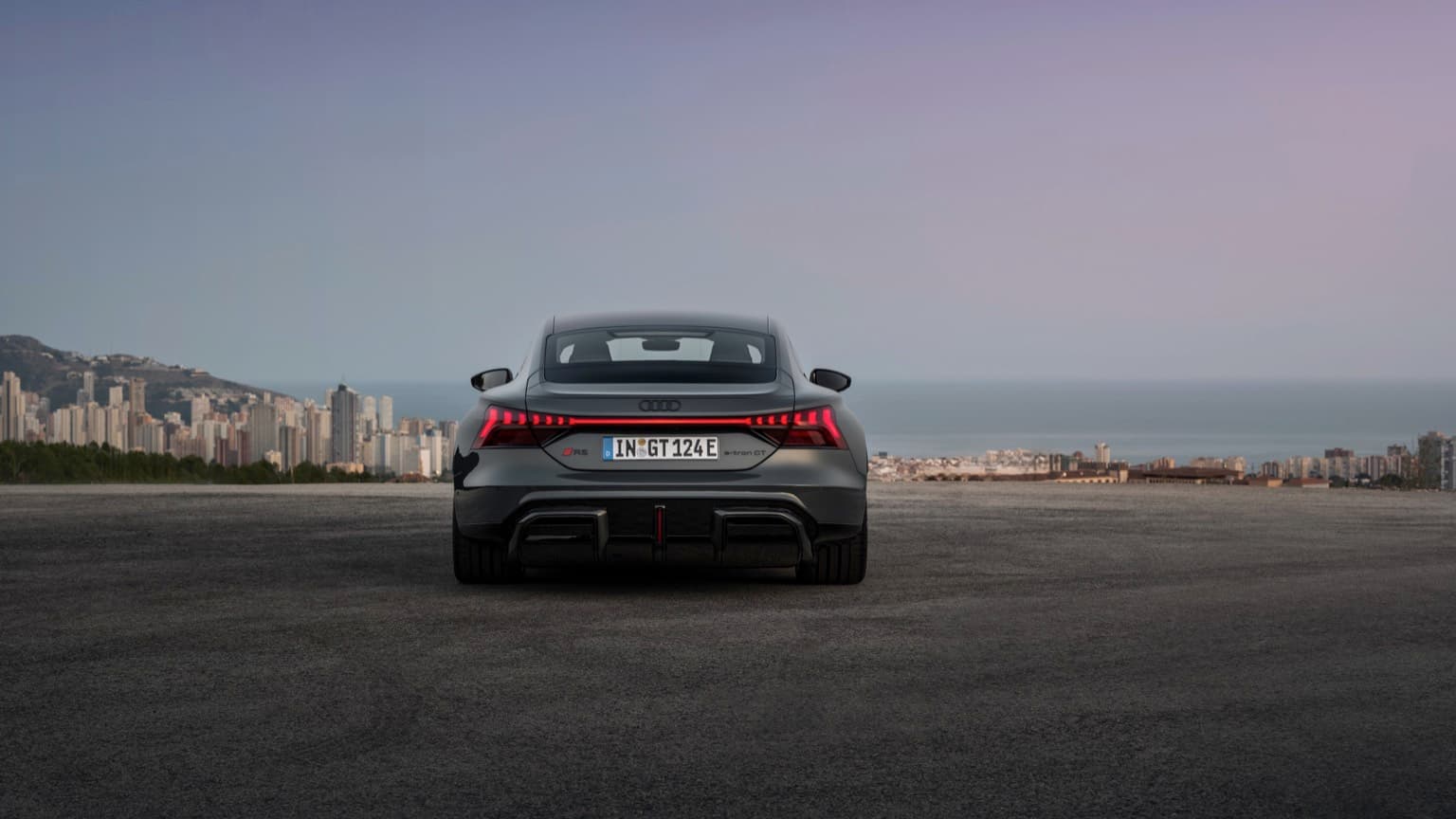 a black sports car on a road with a city in the background
