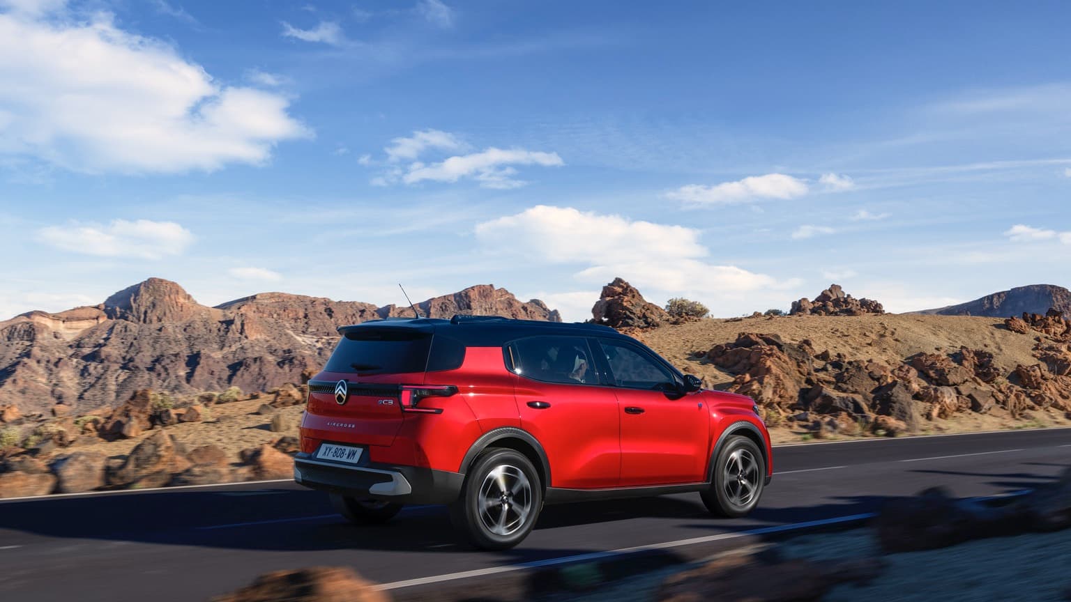 a red car driving on a road with rocky hills in the background