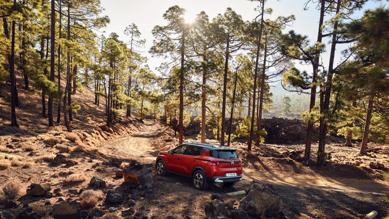 a red car parked on a dirt road surrounded by trees