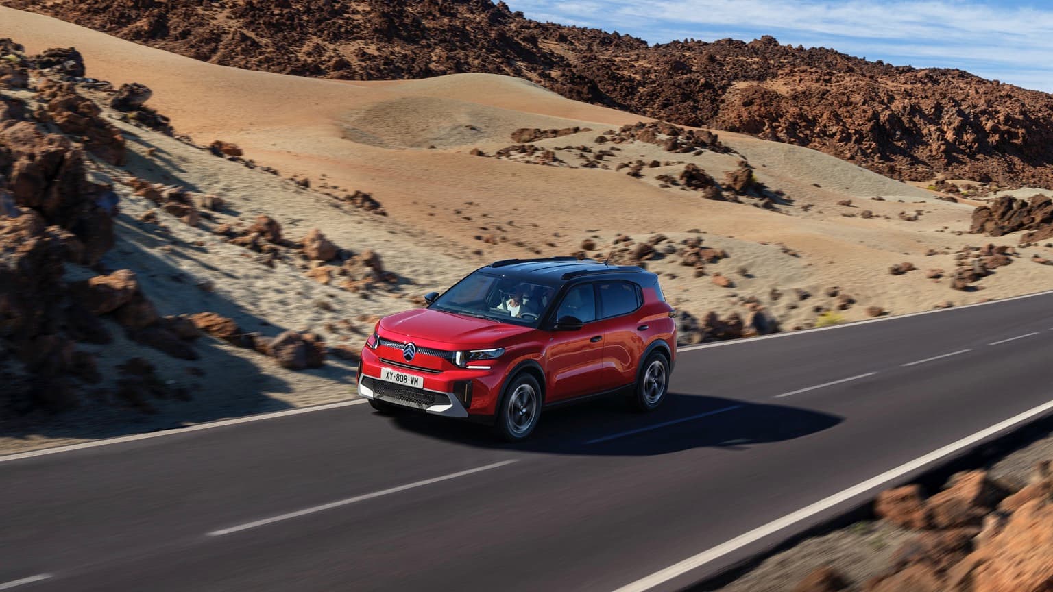 a red car driving on a road with hills in the background