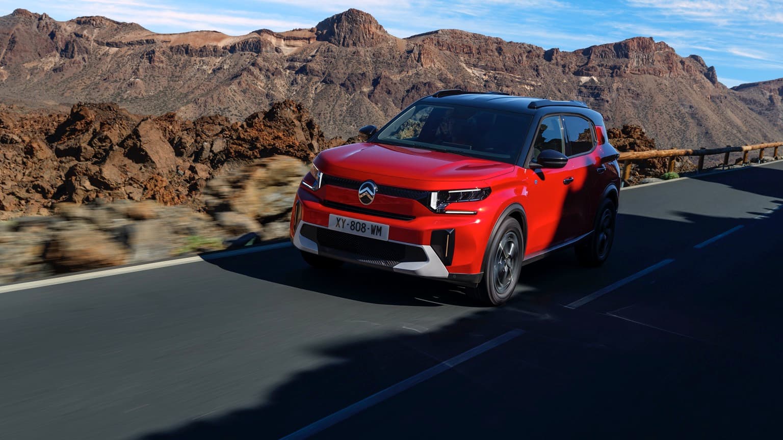 a red car driving on a road with rocky hills in the background