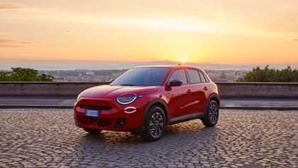 une voiture rouge garée sur une route en briques avec un coucher de soleil en arrière-plan