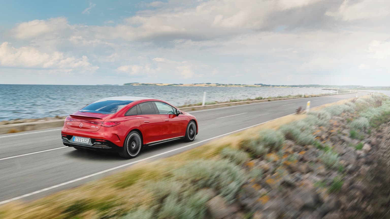 une voiture rouge roulant sur une route au bord de l'eau
