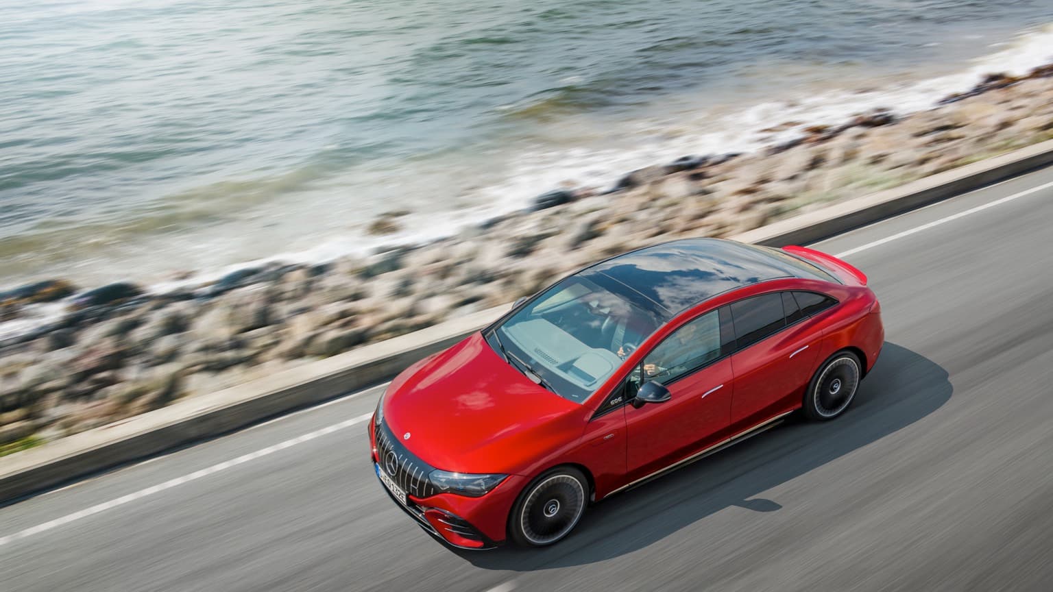 une voiture rouge roulant sur une route au bord de l'eau