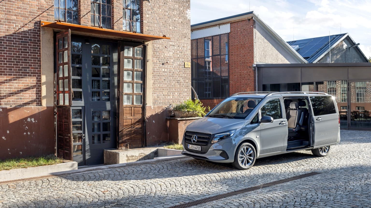 une camionnette grise aux portes ouvertes devant un bâtiment en briques