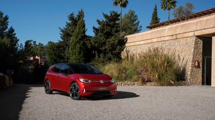 une voiture rouge garée sur du gravier près d'arbres