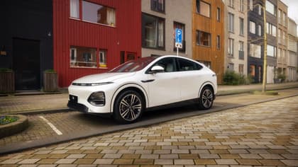 une voiture blanche garée sur une route en briques à côté d'un bâtiment rouge