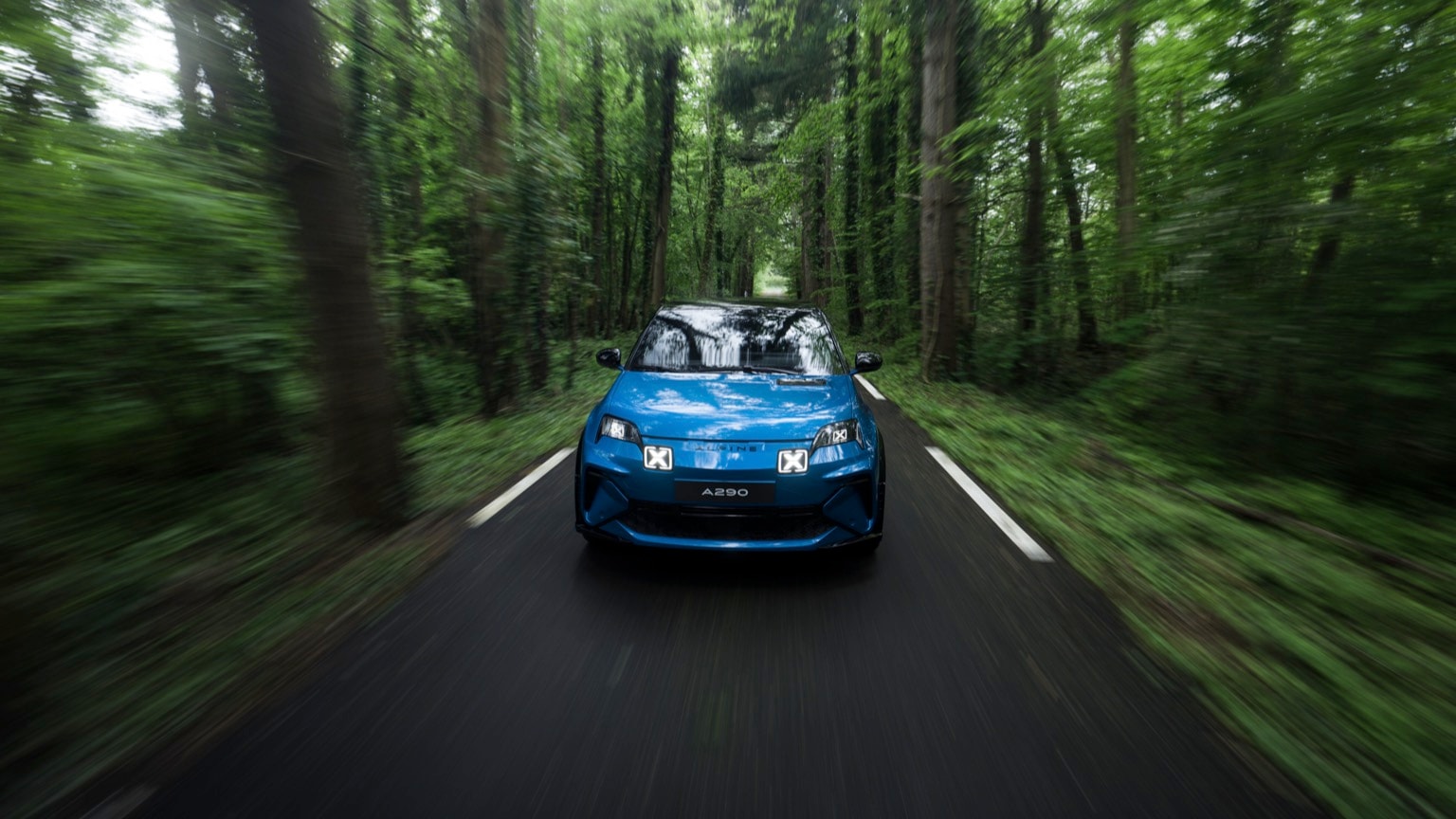 a blue car driving on a road through a forest