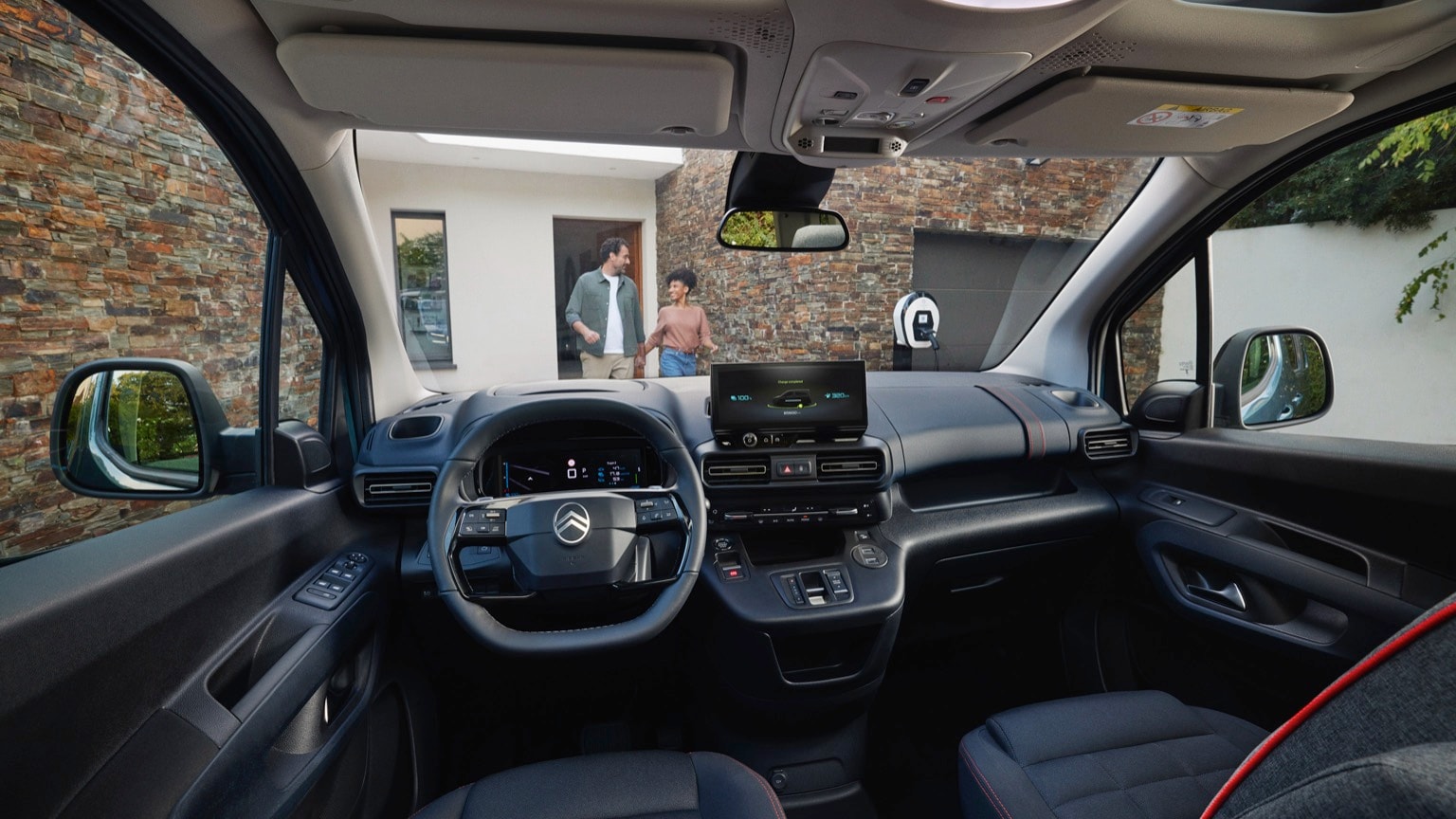 à l'intérieur d'une voiture avec un volant et un homme et une femme debout à l'arrière-plan