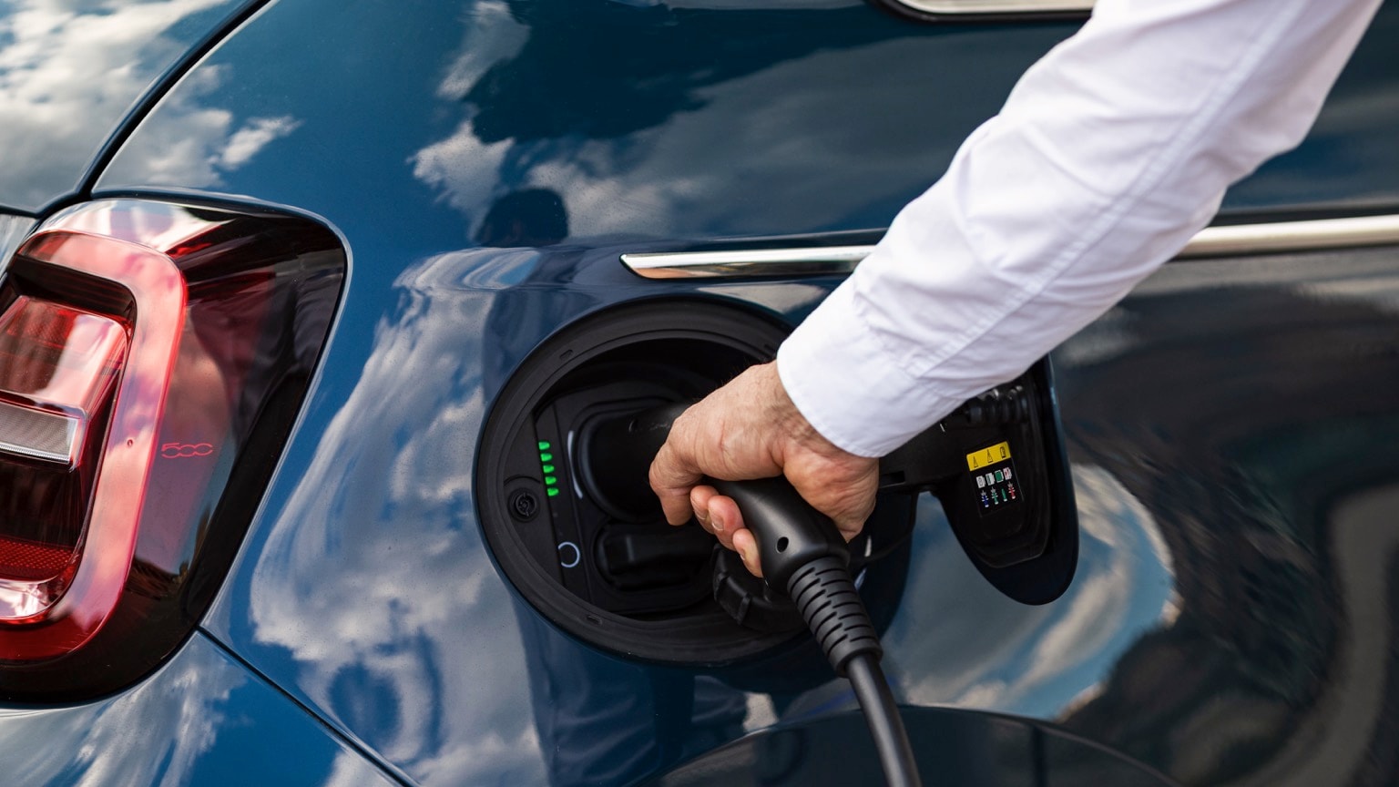 a person holding a black cable to a car