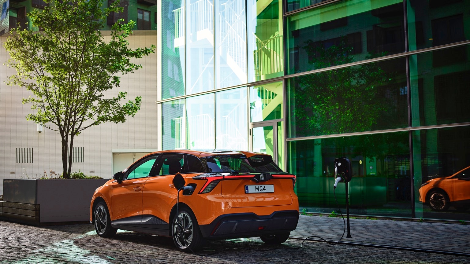 an orange car parked in front of a glass building