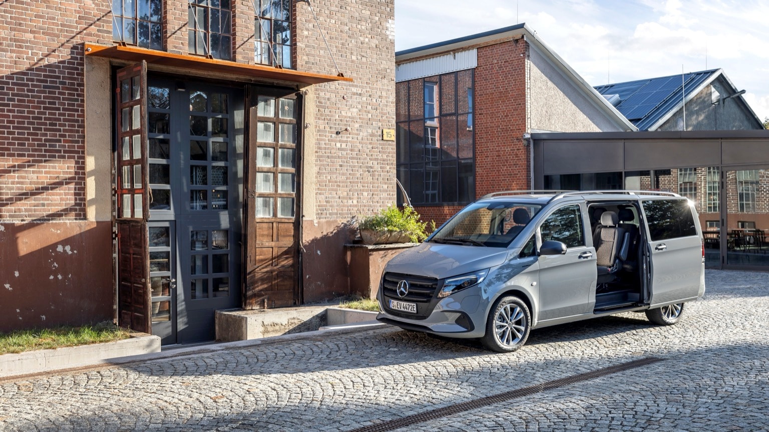 une camionnette grise aux portes ouvertes devant un bâtiment en briques