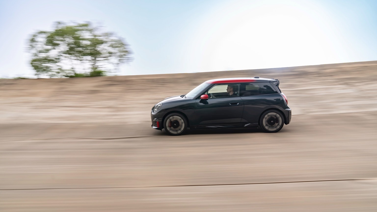 a black car with red roof driving on a dirt road