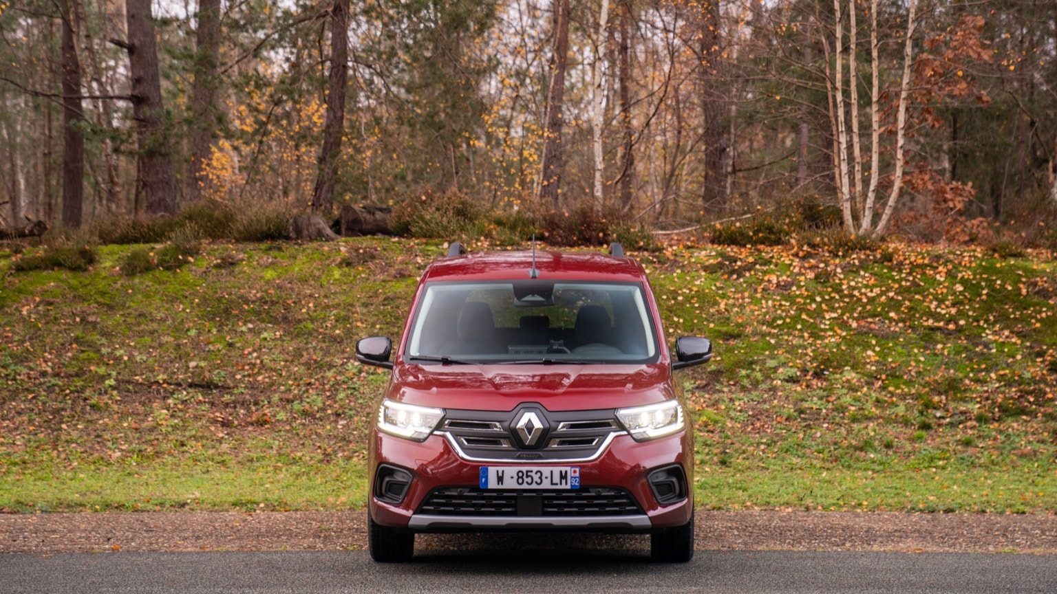 une voiture rouge garée sur une route avec des arbres en arrière-plan