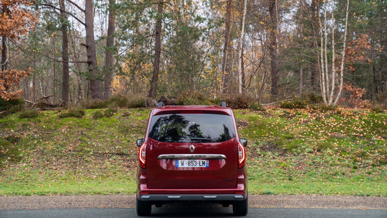 une voiture rouge garée sur une route avec des arbres en arrière-plan