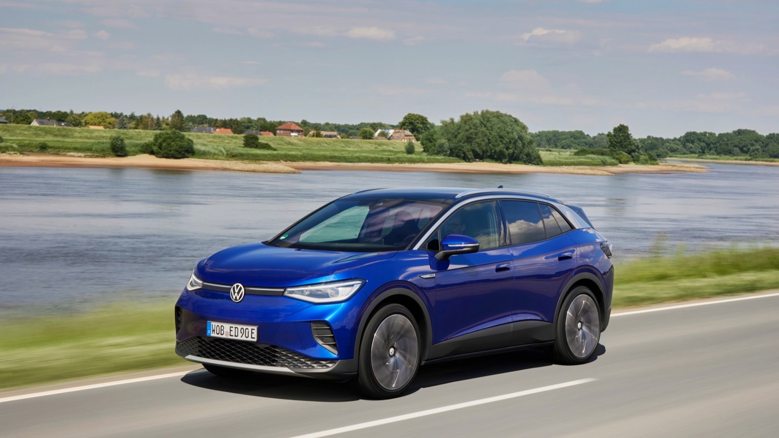 une voiture bleue roulant sur une route près d'une étendue d'eau